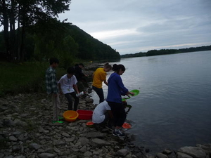 キャンプ地の川岸で皿洗いをしている様子の写真