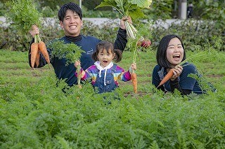 写真：後藤農園 後藤幸治さんと女性と女の子が人参を手にもって収穫している様子